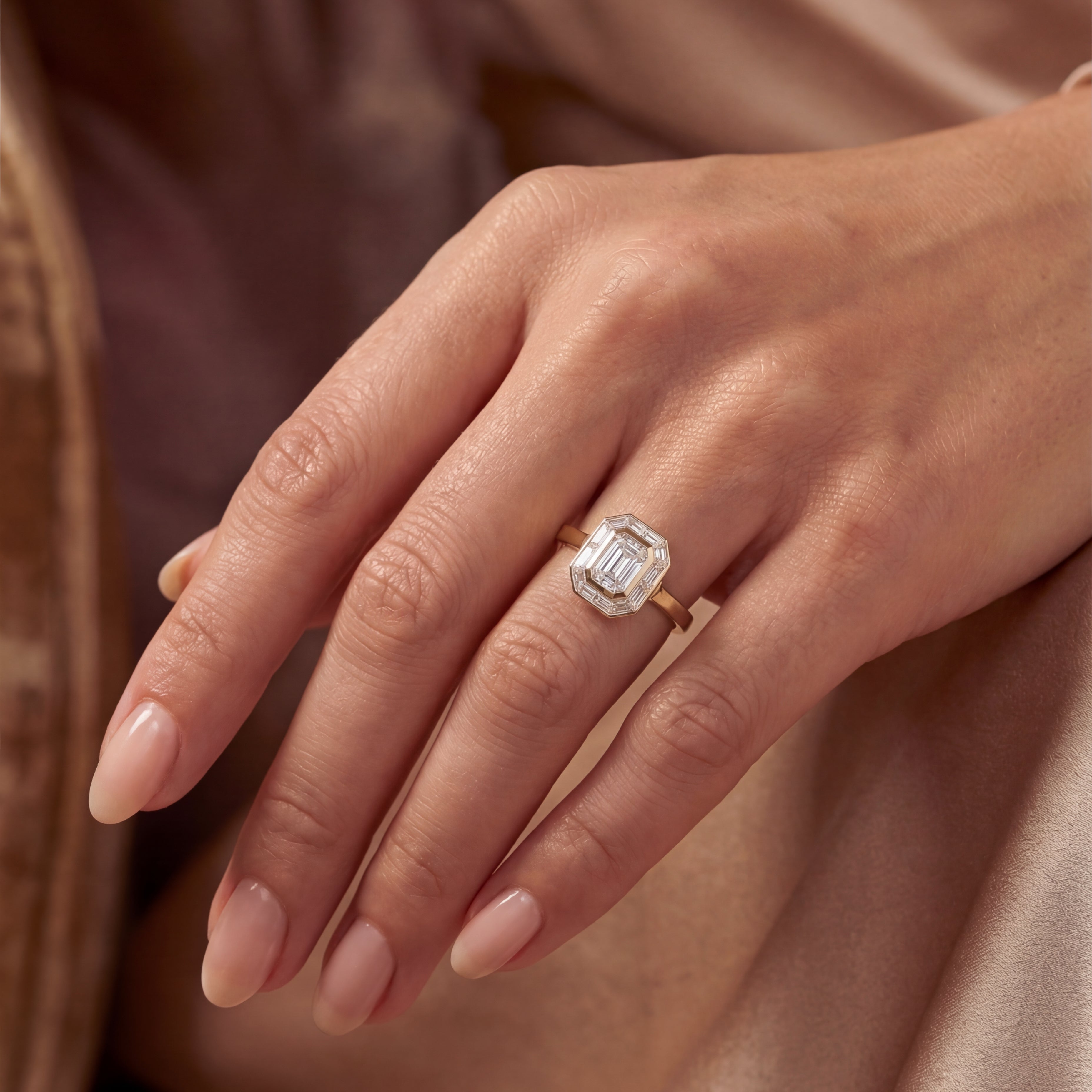 Art Deco inspired engagement ring on hand with emerald cut diamond centre stone set in yellow gold.
